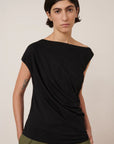 asymmetric top in black on a model with green pants on a cream background