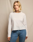 Woman wearing a white long-sleeve shirt and blue jeans against a beige background, size L
