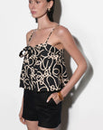 Woman wearing a black and beige patterned top with black shorts on a white background