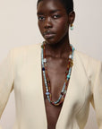 A model wearing a cream-colored blazer, Mini Organic Hoops in Seafoam and a long, multi-strand beaded necklace with turquoise, blue, brown, and gold beads, set against a plain beige background.