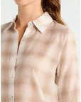A close-up of a woman wearing a light beige button-up shirt with a subtle textured pattern, showing the collar, buttons, and upper chest area against a plain light background.
