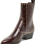 A dark brown leather ankle boot with a pointed toe, a low block heel, and decorative gold-tone studs along the shaft and side panels, shown against a plain white background.
