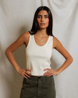 Woman wearing a white tank top and green pants against a plain background
