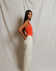 Woman wearing an orange top and white pants against a plain background