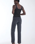 A model is shown from the back wearing a black studded halter top, dark gray jeans, and black high heels against a plain white studio background.