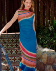 Woman in a colorful striped dress standing outdoors near decorative steps and plants.
