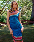 Woman wearing a colorful dress standing outdoors with trees and a fence in the background