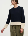Person wearing a navy sweater with beige cuffs and hem on a white background