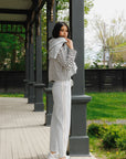 Woman standing on a wooden porch wearing a striped sweater and light pants.