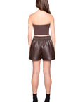 Woman wearing a brown strapless top and leather shorts on a white background back view