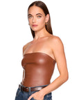 A woman modeling a strapless, glossy brown faux-leather tube top paired with blue jeans and a brown belt, shot against a solid white background.