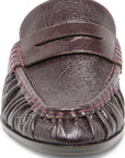 A close-up of a dark brown leather moccasin loafer with a textured leather strap and gathered footbed, featuring pink contrast stitching.