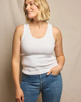 Woman size L wearing a white tank top and blue jeans against a beige background