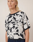 Woman wearing a black and white floral patterned top against a plain background