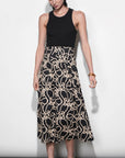 Woman wearing a black sleeveless top and patterned skirt against a white background