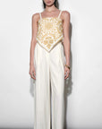 Woman wearing a white outfit with gold lace top against a white background