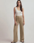 Woman wearing a white tank top and beige pants on a plain background, front view