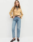 Woman wearing a beige blazer, plaid shirt, and blue jeans on a white background