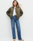 Person wearing a green quilted jacket and blue jeans on a white background