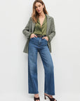Woman wearing a green blazer, green top, and blue jeans on a white background