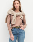 Woman wearing a beige sweater, scarf, and blue jeans against a white background