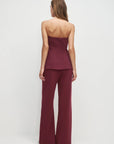 Woman wearing a burgundy strapless top and wide-leg pants on a white background