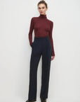 Person wearing a burgundy turtleneck and navy pants on a white background
