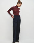 Woman wearing a burgundy turtleneck and navy pants on a white background