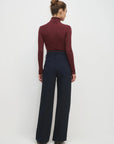 Person wearing a burgundy turtleneck and navy high-waisted pants on a white background