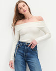 Woman wearing a white off-shoulder top and blue jeans against a white background