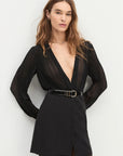 Woman wearing a black dress with a plunging neckline and long sleeves on a white background