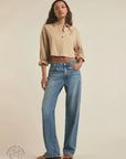 Woman wearing a beige shirt and blue jeans on a plain background