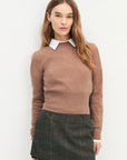 Woman wearing a brown sweater with a white collar and a plaid skirt on a white background