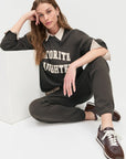 model wearing collegiate sweatshirt with brown pants and brown shoes sitting on the ground with a white background