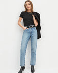 Woman wearing a black t-shirt, light blue jeans, and black boots on a white background