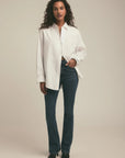 Woman wearing a white shirt and blue jeans against a beige background, full body front