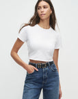 Woman wearing a white t-shirt and blue jeans against a plain background