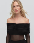 Woman wearing a black off-shoulder top against a plain background