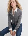 Woman wearing a gray cardigan with red buttons and jeans on a light gray background