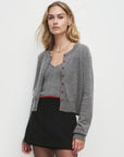 Woman wearing a gray cardigan with red buttons and matching tank over a black skirt on a white background