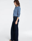 Woman wearing a blue sweater and dark blue wide-leg pants on a white background, side