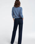 Person wearing a blue sweater and dark pants on a white background, back