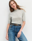 Woman wearing a gray sweater and blue jeans with The Suede Statement Belt in Chocolate against a white background