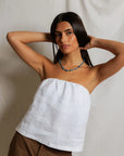 Woman wearing a white strapless top and brown pants against a plain background