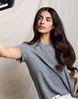Woman taking a selfie wearing a gray t-shirt against a plain background