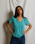 model wearing a teal tee with jeans on a cream background
