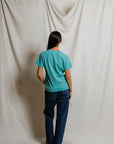 model wearing a teal tee with jeans on a cream background, back