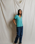 model wearing a teal tee with jeans on a cream background