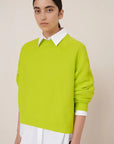Person wearing a bright green sweater over a white shirt on a beige background