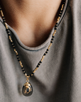 Necklace with black beads and gold accents worn by a person in a gray shirt.